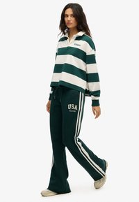 Groen en witte gestreepte pullover met kraag, gecombineerd met groene sweatpants met witte zijkanten en "USA"-tekst. Casual pasvorm, zachte stof.