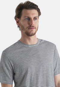 Raidallinen t-paita, joka on valmistettu pehmeästä puuvillasta, esittelee vuorottelevia tummansinisiä ja valkoisia vaakaraitoja. Pyöreä pääntie, jonka reunuksessa on ribbikuviointi, sekä lyhyet hihat.