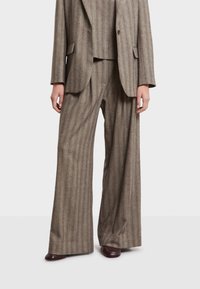 Completo marrone a righe con blazer su misura e pantaloni a gamba larga in un tessuto strutturato. L'outfit presenta una leggera lucentezza e una vestibilità ben definita.