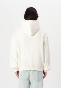 Sudadera oversized color crema con capucha con cordón, puños y dobladillo acanalados. Combinada con jeans de mezclilla claros. Material de algodón suave.