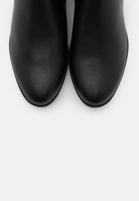 Un paio di scarpe eleganti in pelle nera viste dall'alto su uno sfondo bianco, evidenziando le punte rotonde e lisce.