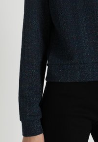 Donkerblauwe cropped sweatshirt met een textuurafwerking, voorzien van spikkels iriserende kleur en aansluitende boorden.