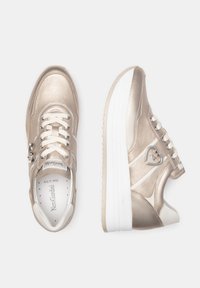 Sneakers métalliques dorés avec des semelles blanches ; dotés de lacets, d'un zip latéral et d'un accent en forme de cœur sur le côté ; texture lisse et design arrondi.