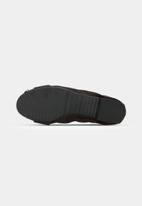 Semelle de chaussure en suède noir avec un motif de rainures texturé, présentant un bout arrondi et un talon plat. Aucun logo ni embellissements visibles.