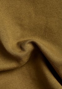 Tejido de punto de color verde oliva con una textura suave y lisa, con un ligero estiramiento. La vista en primer plano resalta las finas y uniformes costuras.