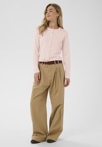 Svetlo roza jopica z okroglim izrezom in gumbi, kombinirana z bež širokimi hlačami, s rjavim pasom.