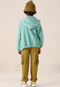 Sweatshirt à capuche bleu clair avec un ourlet élastique, associé à un pantalon cargo moutarde avec des poches latérales et des poignets retroussés, complété par des baskets.