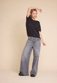 Svart fluffy strikkegenser, vide grå bukser og tykke svarte sko. Antrekket har myke teksturer og løse, avslappede former.