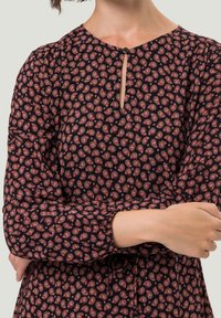 Langärmliges Kleid aus schwarzem Stoff mit rotem Paisley-Muster, einem Schlüssel-Ausschnitt und raffinierten Details an den Ärmeln.