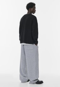 Pulover negru tricotat supradimensionat cu tiv zimțat și pantaloni de trening gri evazați. Pantofi masivi negri, textură de țesătură netedă și design minimal.
