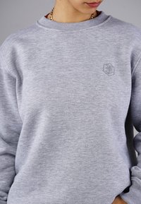 Grauer Kapuzenpullover aus weichem Stoff, mit geripptem Kragen und Bündchen. Gesticktes Logo auf der Brust. Lässige Passform mit leichter Textur.