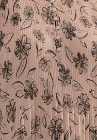 Flydende lyserød bluse med lodrette plisseringer og sort blomstermønster. Har runde knapper ned ad forsiden; glat, let stof.