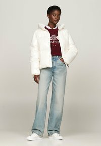 White shiny puffer jacket with a hood, worn over a burgundy sweater, paired with light blue wide-leg jeans and white sneakers.