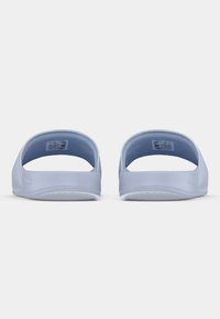 Sandales légères bleu clair à enfiler, avec un dos ouvert, une texture lisse et des semelles plates, présentant un design minimaliste et un marquage subtil sur le côté.