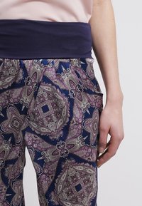 Navy pants with a paisley pattern in purple and cream, featuring a broad, navy waistband. Smooth fabric with a relaxed fit.