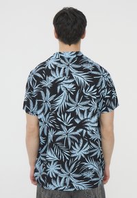 Camisetta a maniche corte con sfondo nero e motivo di foglie di palma tropicali blu. Realizzata in tessuto leggero, design a vestibilità rilassata.