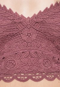 Bralette en dentelle couleur mauve profond, avec broderie florale, bords festonnés et motif texturé sur tout le tissu.