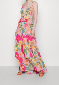 Vestido maxi floral colorido con un profundo escote en V, cintura con volantes, falda en capas y tirantes finos. El material parece ligero y fluido.