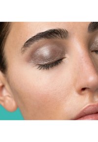 Gros plan sur un œil avec un fard à paupières bronze scintillant, des cils définis et une texture de peau lisse, sur un fond turquoise.