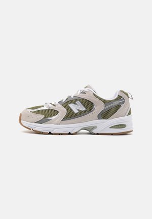Jasnobeżowe i oliwkowozielone buty sportowe New Balance 530 z panelami z siateczki, białymi sznurowadłami i białą, amortyzowaną podeszwą na jednolitym tle.