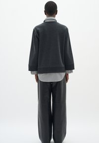 Tmavě šedá oversized mikina s kulatým výstřihem přes černá a bílá pruhovaná košile, doplněná černými širokými koženými kalhotami.