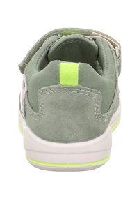 Sneaker in suede verde e tessuto con suola in gomma bianca. Presenta un vivo tab posteriore giallo e una cinghia regolabile. Cuciture rinforzate visibili.