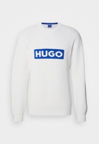 Biały dziergany sweter o prążkowanej fakturze, z wyraźnym niebieskim logo "HUGO" na przodzie i długimi rękawami.