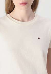 T-shirt di cotone color crema con collo tondo e maniche corte. Presenta un piccolo logo ricamato in rosso, bianco e blu sul petto.