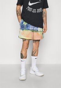 Sort Nike t-shirt med hvidt logo, multicolore mesh shorts med abstrakt print, hvide Nike sokker og hvide sko. Vist fra livet og ned.