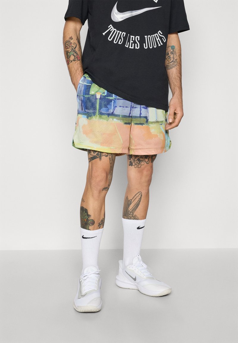 Sort Nike t-shirt med hvidt logo, multicolore mesh shorts med abstrakt print, hvide Nike sokker og hvide sko. Vist fra livet og ned.