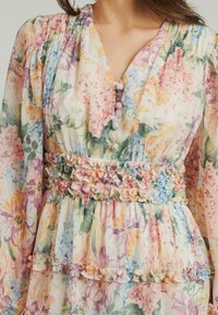 Blumenmusterkleid aus leichtem Stoff in Pastellfarben. Rüschendetails an der Taille und dem Saum, mit sanften Knöpfen und einem V-Ausschnitt.