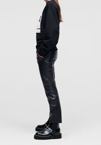 Sudadera negra con gráfico blanco, combinada con pantalones de cuero negros de cintura alta y botas de plataforma negras con cadena.