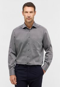 Graues Langarmhemd mit kleinem karierter Muster, Button-Down-Kragen, Brusttasche und schwarzen Knöpfen, kombiniert mit dunklen Hosen.