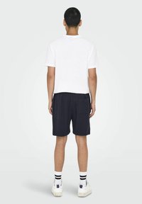 Camiseta de algodón blanca, pantalones cortos negros con un bolsillo, rayas en contraste en calcetines blancos y zapatillas blancas con un acento morado.