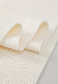 Material din bumbac într-o nuanță albă-crem, care pune în evidență o textură striată și margini moi, pliate, subliniind o suprafață netedă și uniformă.