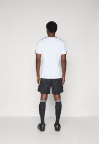 Bílý sportovní dres s černými akcenty, černé kraťasy s zeleným a červeným prošíváním, černé ponožky do stehen a černé kopačky.