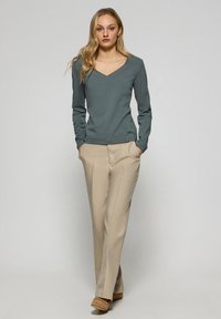 Långärmad, v-ringad topp i skifferblått tyg, tillsammans med beige skräddarsydda byxor, som har stilrena linjer och en bekväm passform.