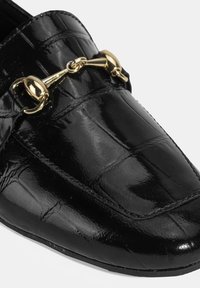 Zwarte patenten leren instappers met een gegraveerd krokodillenpatroon, voorzien van een goudkleurig hardwareaccent aan de voorkant. Klassiek elegante uitstraling.