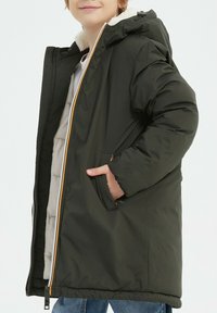 Doudoune vert foncé avec fermeture éclair à l'avant, capuche doublée en fourrure et poches latérales, avec des accents orange et une doublure intérieure douce.