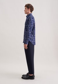 Granatowa koszula w kwiaty z kołnierzykiem na guziki, długimi rękawami i prostym krojem, zestawiona z wąskimi ciemnymi spodniami i czarnymi eleganckimi butami.