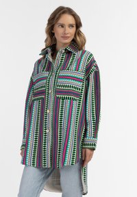 Marškiniai su daugiaspalviu raštu, kuriame yra žali, rožiniai ir mėlyni dryžiai, du priekiniai kišeniai ir ilgesnis nugaros krašto dizainas.