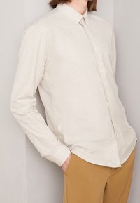 Lichtbeige overhemd met lange mouwen en knopen in een zachte, gestructureerde stof, met een klassieke kraag en subtiele stikseldetails, gedragen met tan kleurige broek.