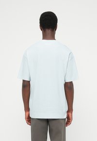 Ανοιχτό μπλε βαμβακερό μπλουζάκι με στρογγυλή λαιμόκοψη, κοντά μανίκια και άνετη γραμμή, που δείχνει μια λεία υφή και μίνιμαλ σχεδιασμό στην πλάτη.