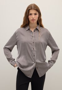 Blouse rayée noir et blanc, avec un devant à boutons, un col, des manches longues et une coupe décontractée avec une texture de tissu lisse.