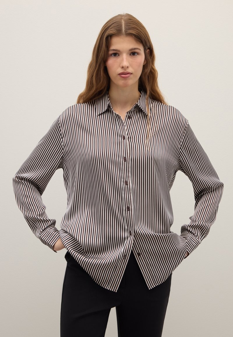 Blouse rayée noir et blanc, avec un devant à boutons, un col, des manches longues et une coupe décontractée avec une texture de tissu lisse.
