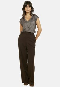 Top grigio scintillante a maniche corte con dettaglio annodato sul davanti, abbinato a pantaloni a palazzo a vita alta di colore marrone scuro. Tessuto liscio e strutturato.