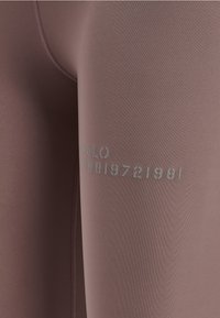 Hoge taille sportleggings van mauve stof. Kenmerken zijn reflecterende tekst "HALO 36819721981" op de zijkant en een gladde, rekbare textuur.