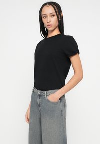 Fekete rövid ujjú, kerek nyakú, pamutból készült póló. Világosszürke, bő szárú farmerrel viselve, amelynek klasszikus derékrésze és zsebei vannak.