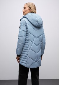 Lichtblauwe pufferjack met capuchon, chevron-gequilt patroon en zwarte accenten op de mouwen. Gladde textuur met een licht matte afwerking.