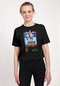 Zwart T-shirt met een kleurrijke afbeelding van gepixelde worstelaars en de tekst "YOU CAN'T SEE ME". Het shirt heeft meerdere logo's en een retro ontwerp.